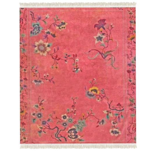 The Rug is a rectangular pink velvet piece with fringed edges, showcasing an intricate floral pattern. It features swirling vines and assorted flowers in blue, yellow, and green on a vibrant pink background.