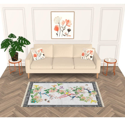 A modern living room features a velvet sofa adorned with floral pillows, a handmade rug with colorful patterns on the herringbone floor, and a floral painting above. A large green plant and two round side tables elegantly flank the sofa.