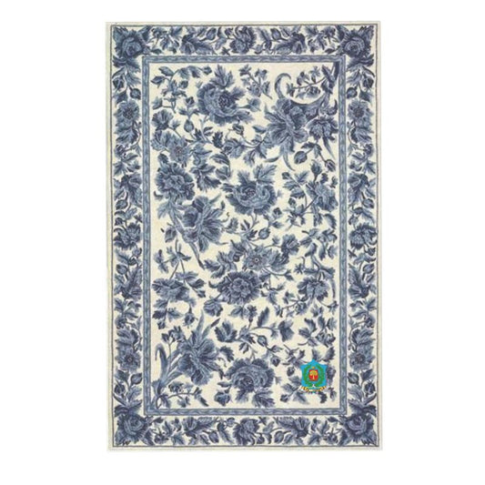 This Rug showcases detailed blue floral designs on a white background, crafted from heavyweight velvet. The border features a dense floral pattern with an anti-slip backing for safety, while a circular logo with a green ribbon is displayed at the bottom right corner.