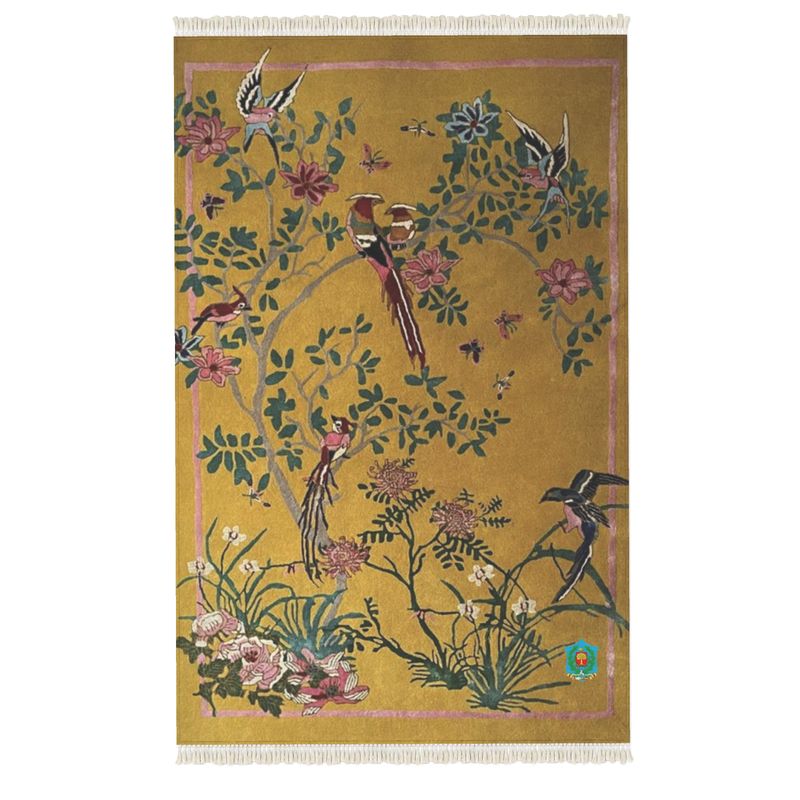 A decorative rug by a renowned designer showcases birds, pink, red, and purple flowers on tree branches against a mustard yellow backdrop. It features fringed edges and anti-slip backing.