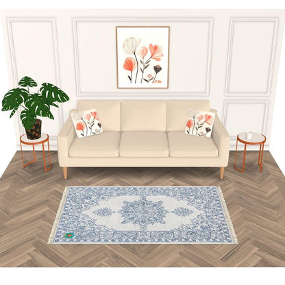 A stylish living room features a beige sofa with floral cushions, matching side tables, and a light blue and white patterned rug with an anti-slip base on chevron wood flooring. The cohesive space is enhanced by potted plants and framed floral artwork.